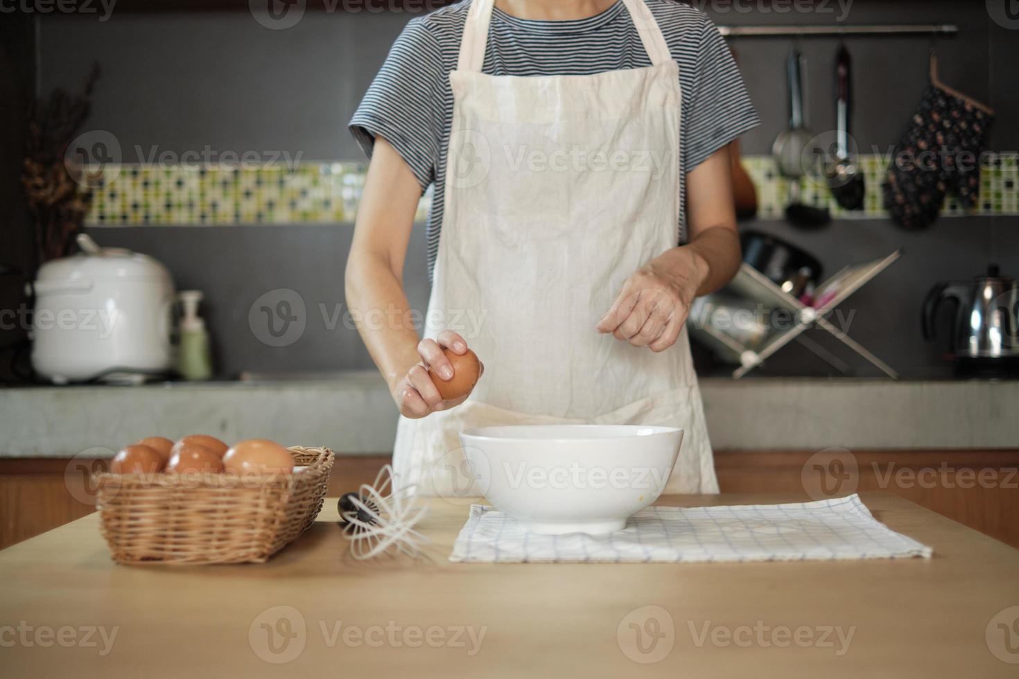 Female cook in a white apron is cracking an egg in home's kitchen. photo