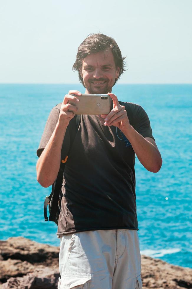 Sonriente hombre feliz, tomando fotos contra el mar azul