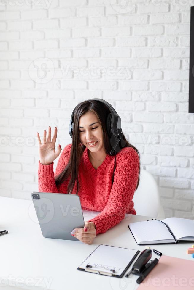 Young woman in black headphones teaching english online using tablet photo