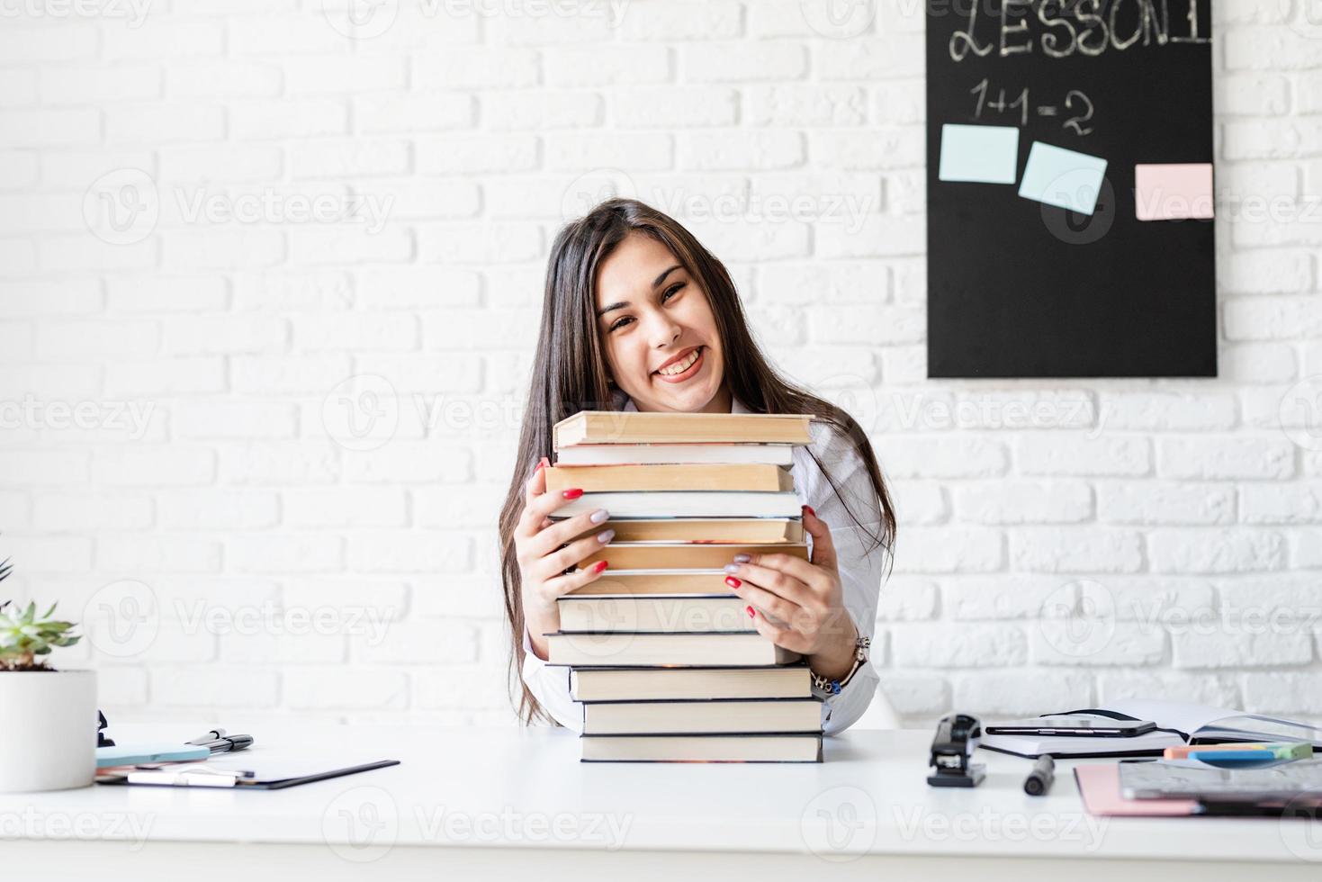 Young teacher sitting with pile of books looking away ready for lesson photo