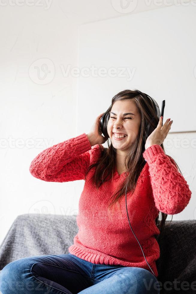 mujer en suéter rojo y auriculares negros sentada en el sofá bailando foto