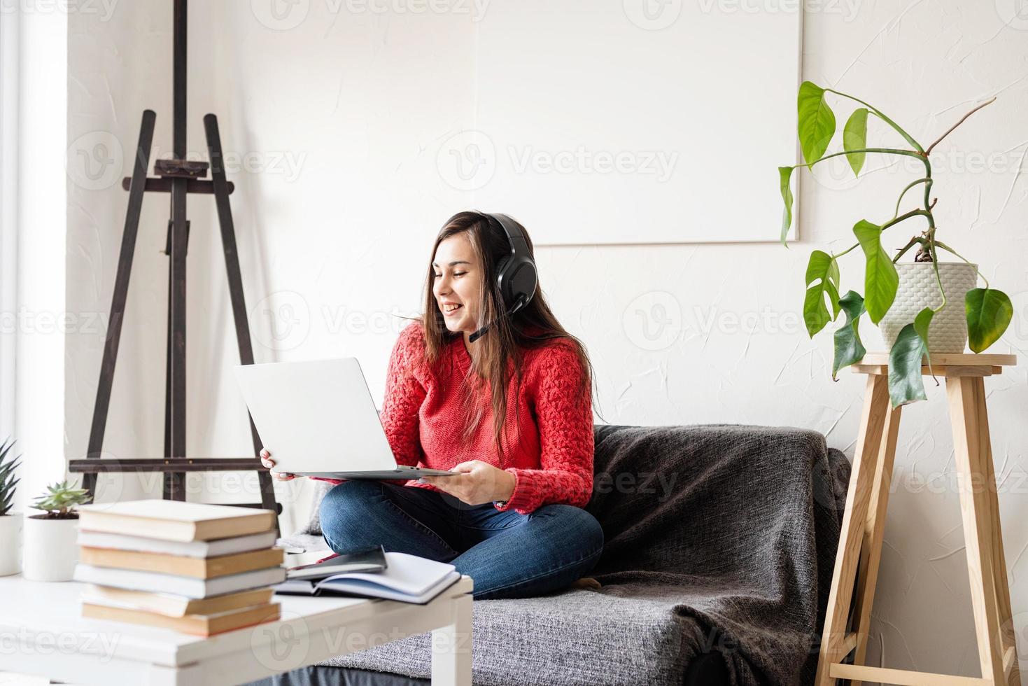 Mujer en suéter rojo y auriculares negros sentada en el sofá foto