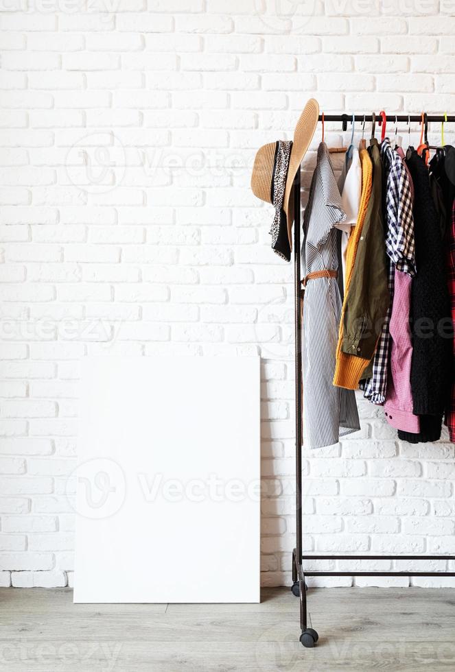 Rack with colorful clothes on hangers and frame canvas for mock up photo