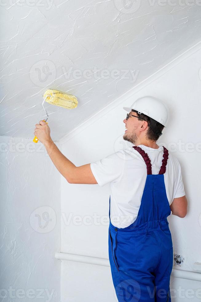 Joven con un mono azul y un casco blanco pintando la pared foto