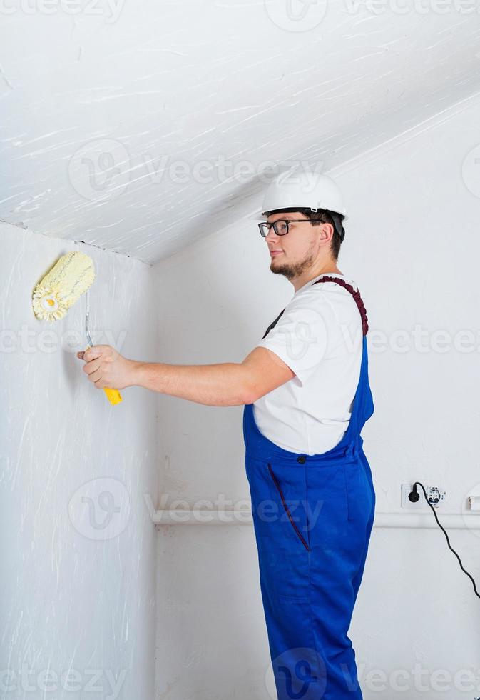 Joven con un mono azul y un casco blanco pintando la pared foto