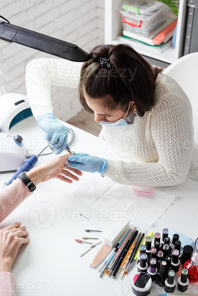 maestro de manicura usando pinzas para hacer manicura a un cliente foto