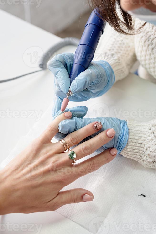 maestro de manicura usando una máquina eléctrica para pulir las uñas foto