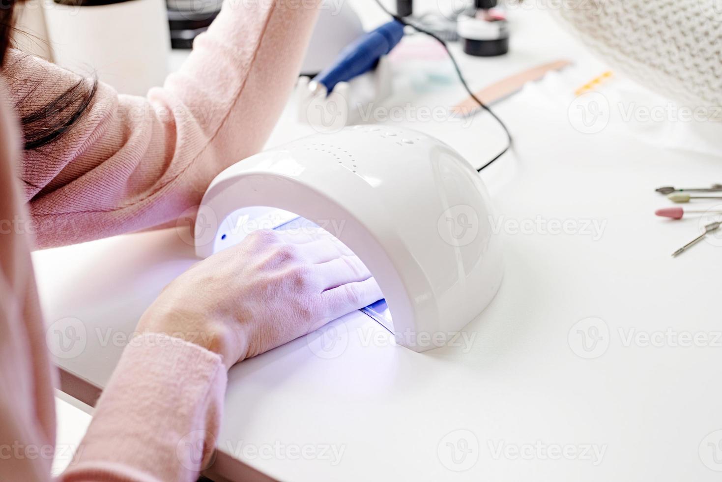 Woman in manicure salon drying her nails in a UV lamp photo