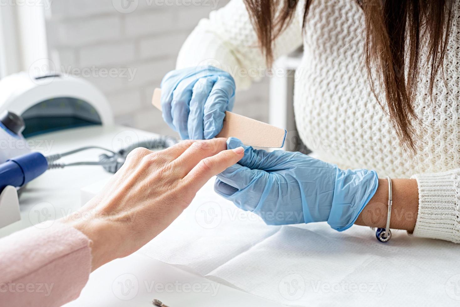 maestro de manicura con lima de uñas para pulir la uña de un cliente foto