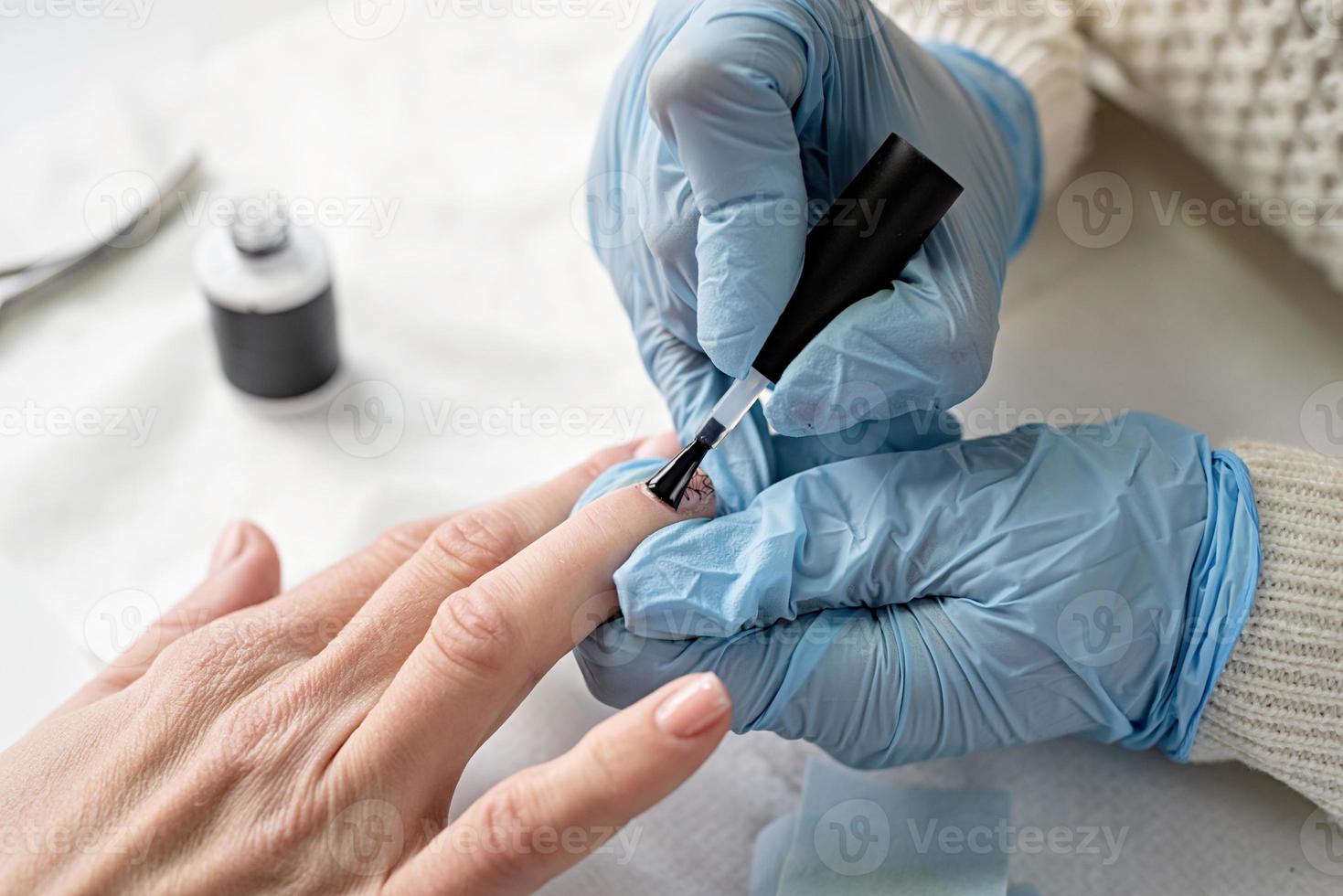 Maestro de manicura en máscara y guantes poniéndose esmalte en gel foto