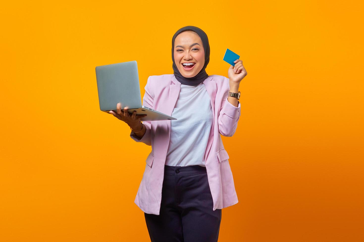 Cheerful asian woman holding laptop and showing credit card photo