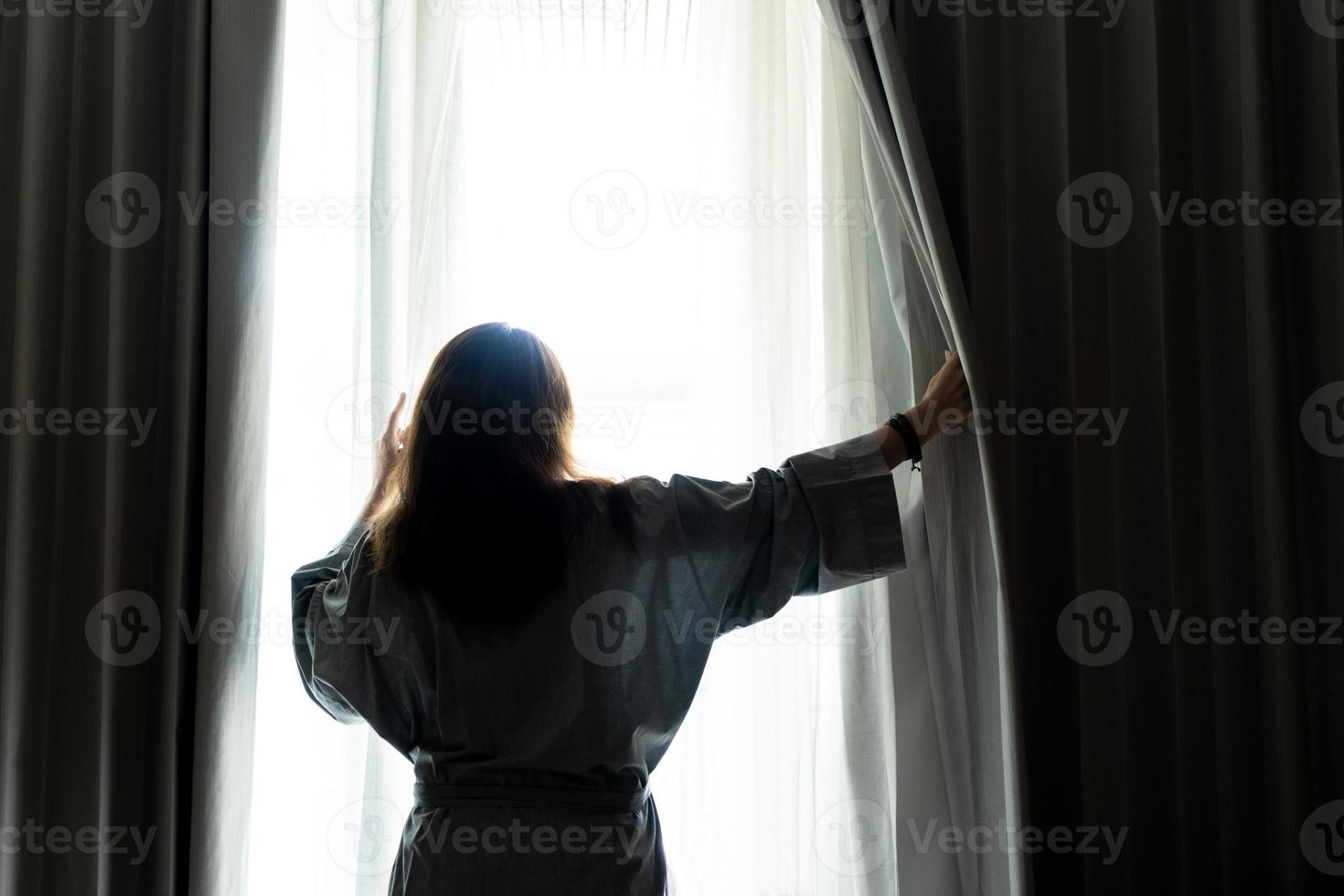 Beautiful woman is opening the curtain at the window in the morning photo