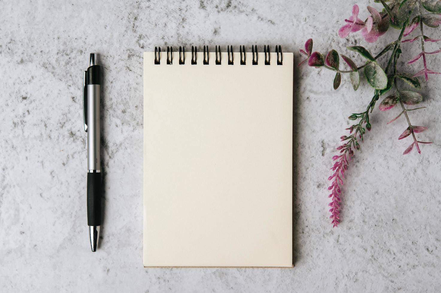 Cuaderno, bolígrafo y flor se coloca sobre fondo blanco. foto