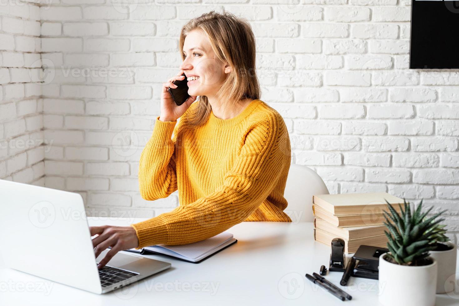 Young woman in yellow sweater using laptop and calling on the phone photo