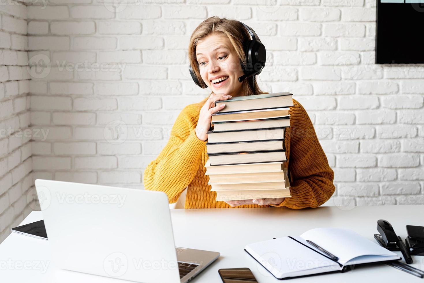 Mujer en auriculares negros estudiando en línea sosteniendo una pila de libros foto