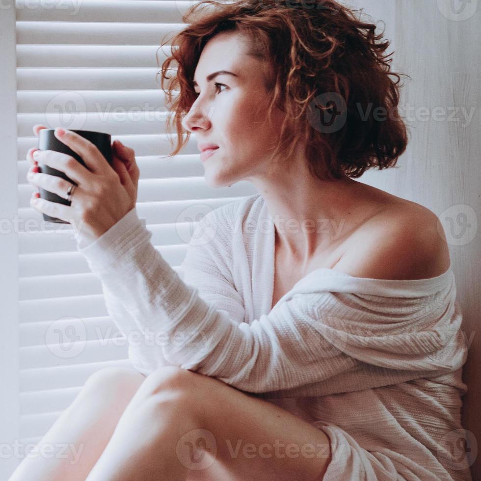 Mujer por ventana con taza, relajación matutina desenfoque de movimiento de luz suave foto