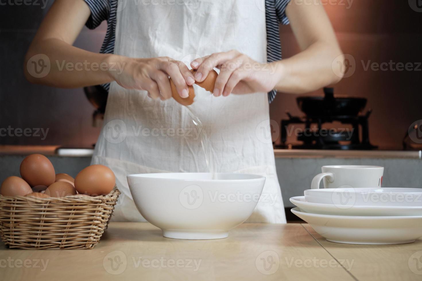 Female cook in a white apron is cracking an egg in home's kitchen. photo