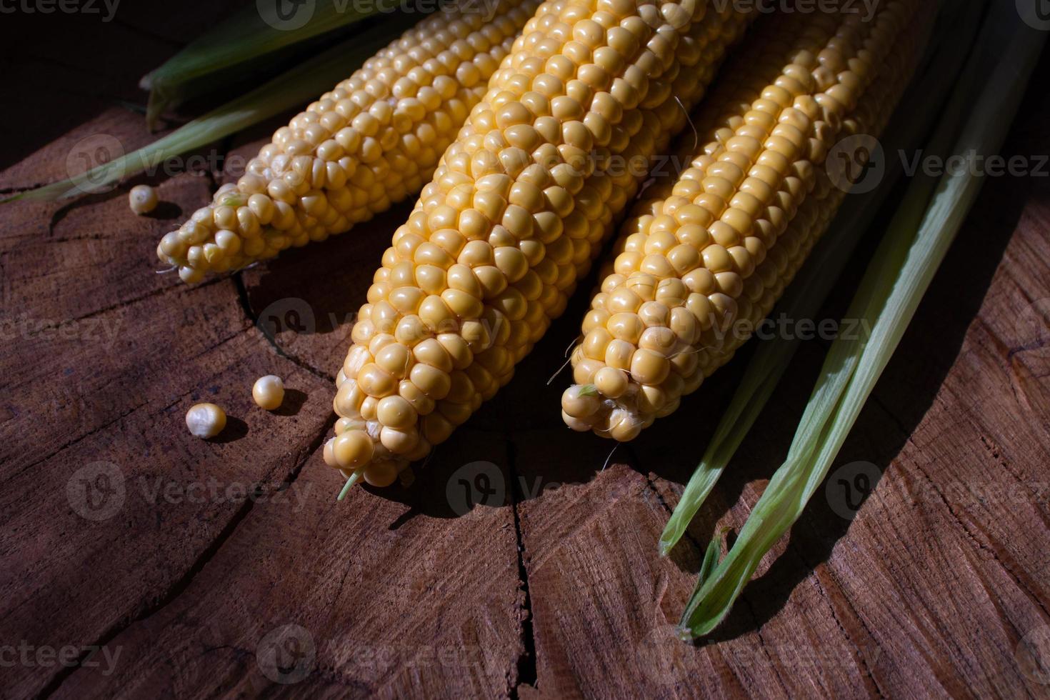 mazorcas de maíz con hojas sobre fondo de madera. comida vegetal fresca foto