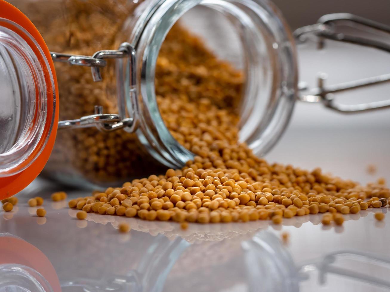 Dry mustard seeds in a glass bottle and a pile of mustard, macro photo