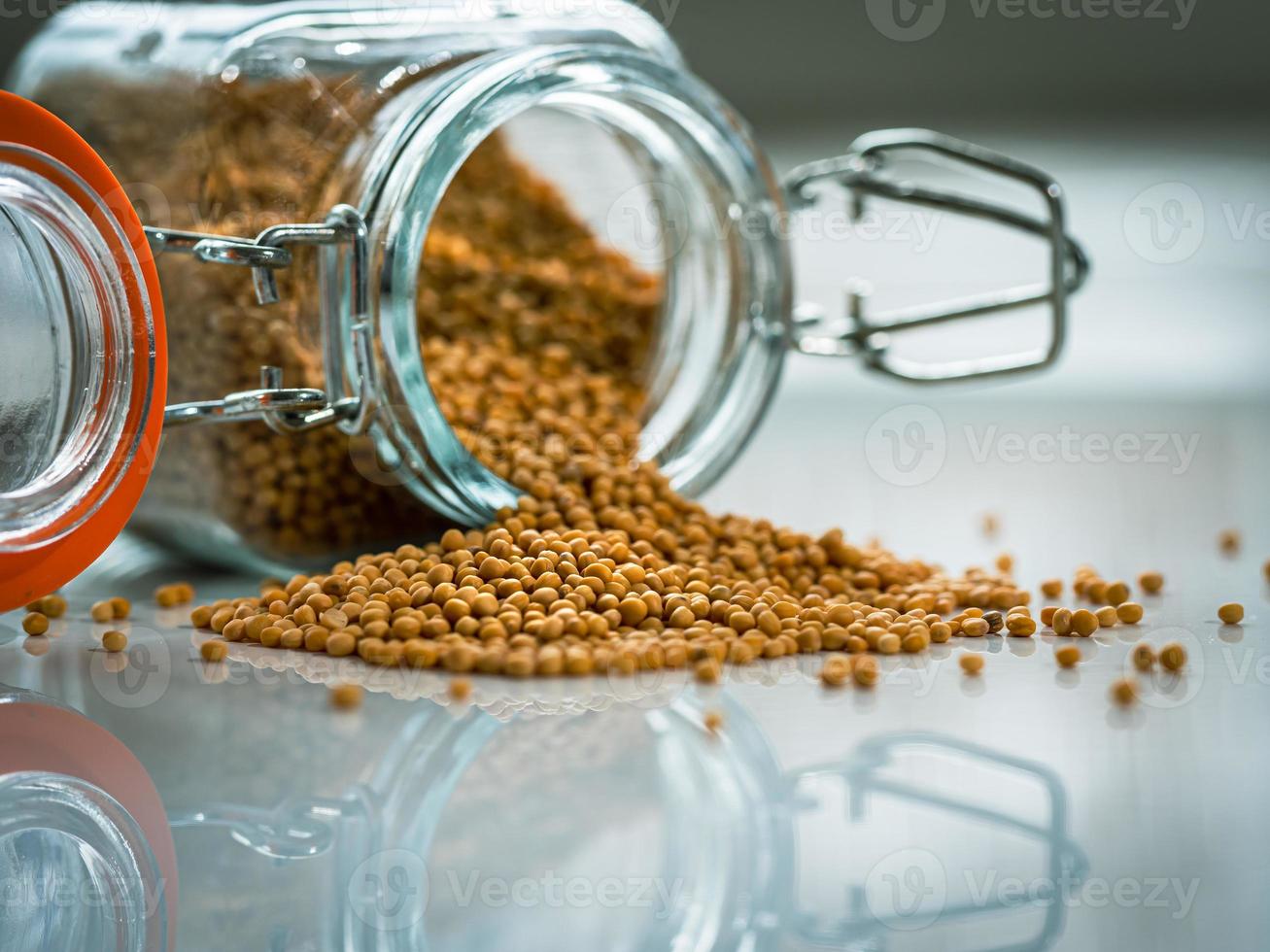 Dry mustard seeds in a glass bottle and a pile of mustard. Macro photo