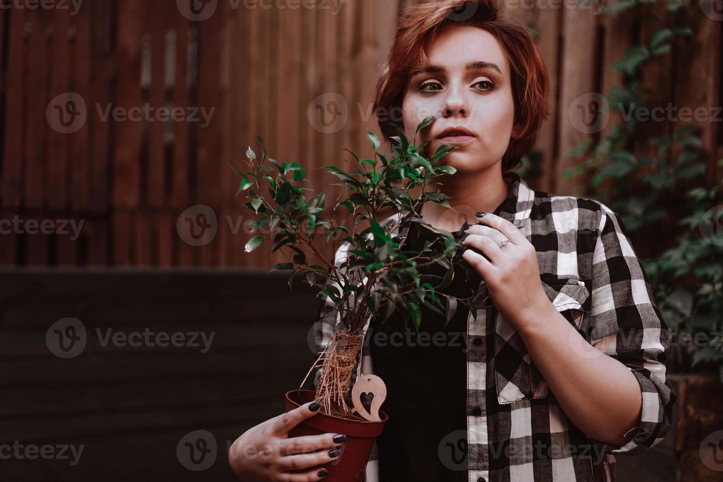 Woman with short red hair in plaid shirt holding a flower in pot photo