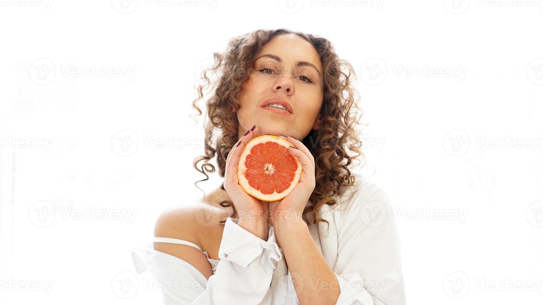 Portrait of pretty middle-aged woman with curly hair with grapefruit photo