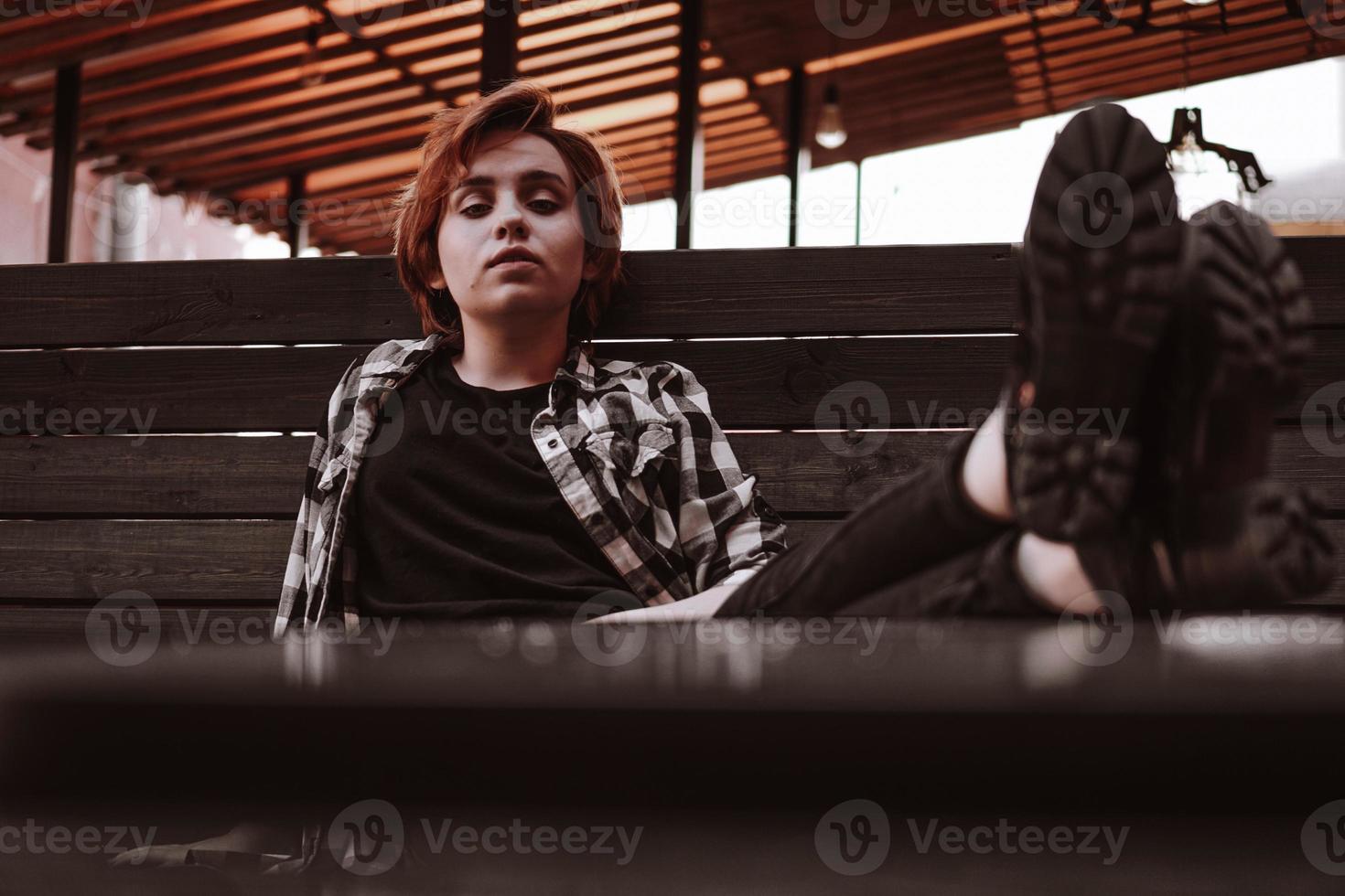 Young woman with short red hair in a bar put her legs on table photo