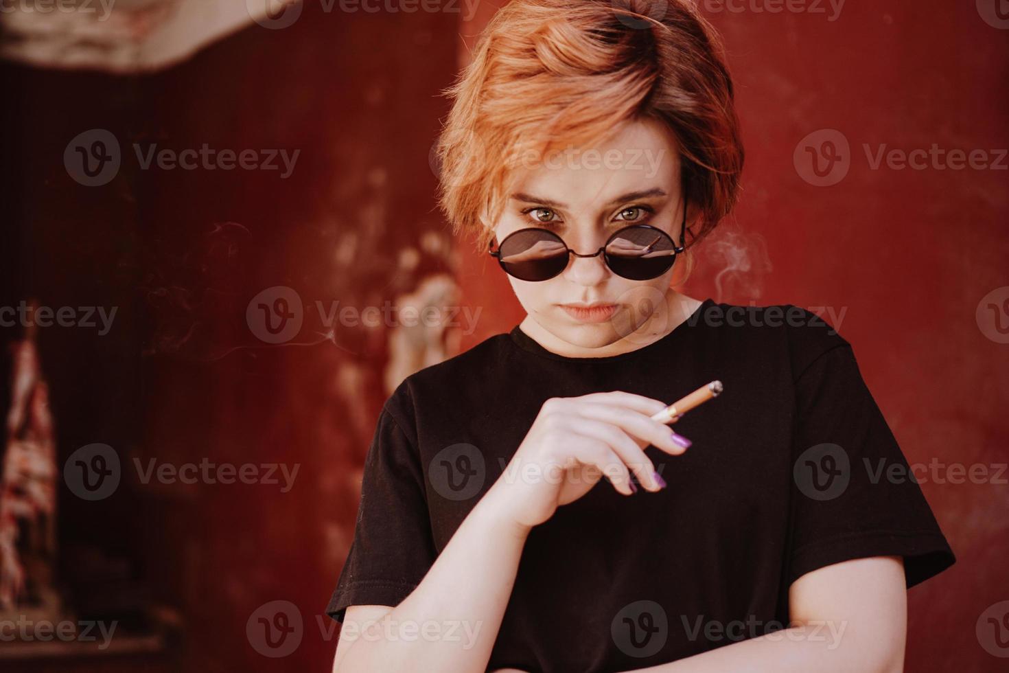 chica con pelo rojo corto y gafas de sol de espejo fumando cigarrillo foto