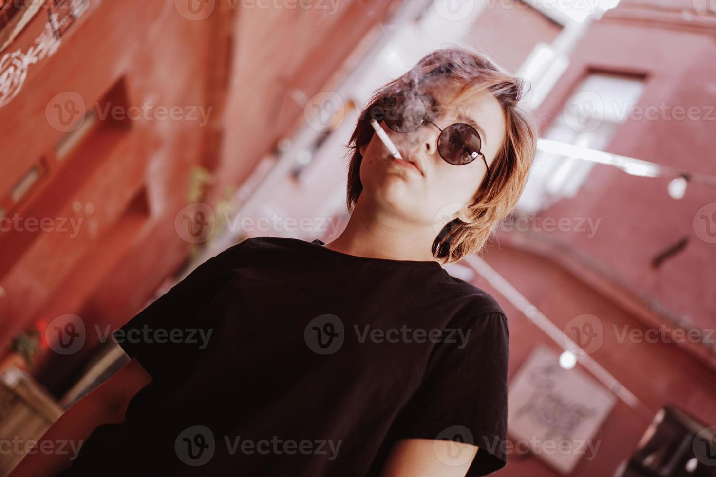 chica con pelo rojo corto y gafas de sol de espejo fumando cigarrillo foto