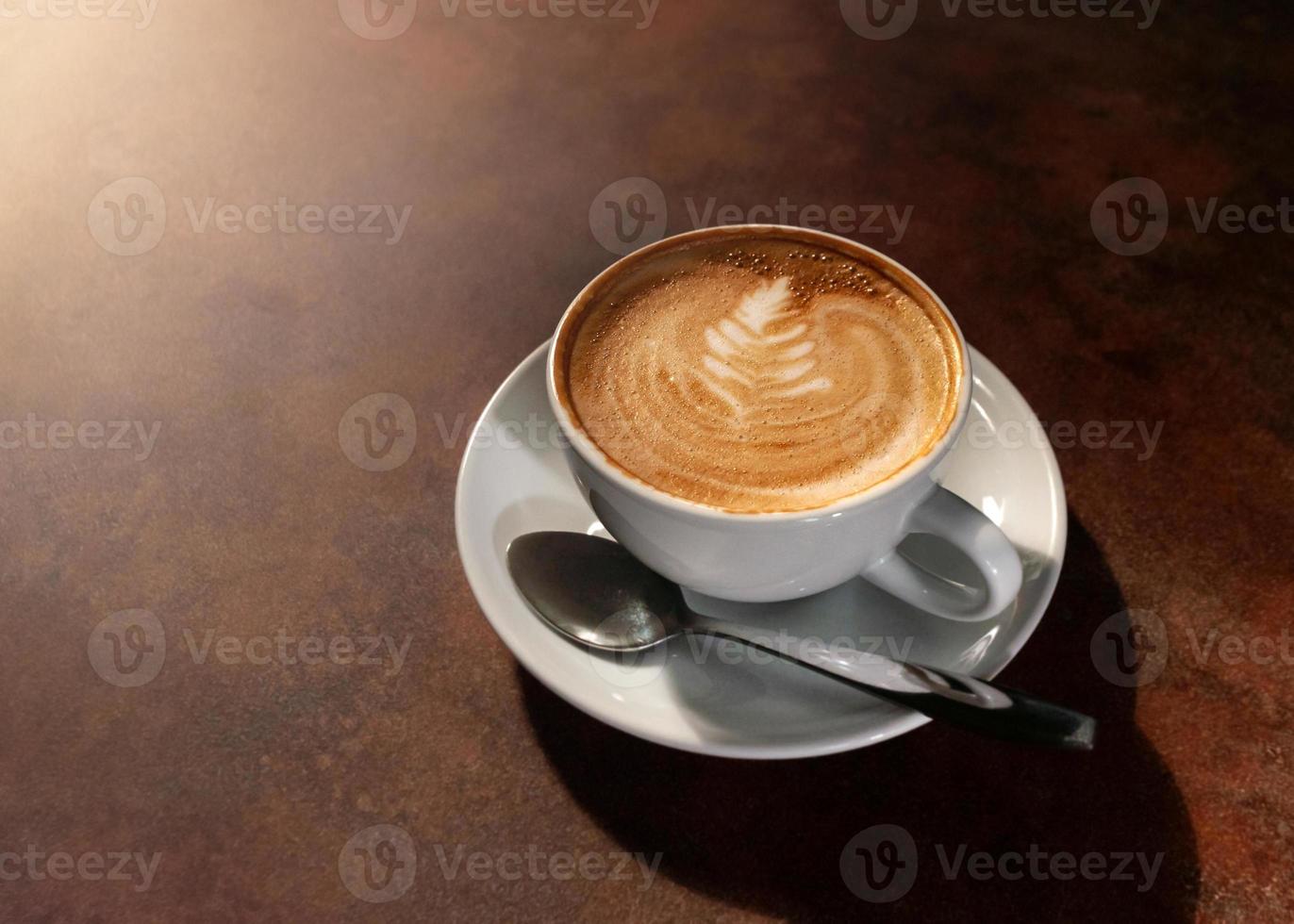 Taza de arte latte caliente en la luz de la tarde en la mesa de madera foto