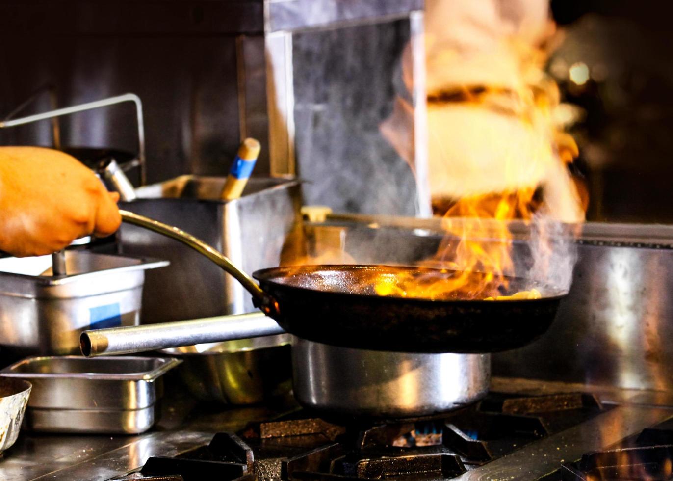 Chef cooking with flame in a frying pan on a kitchen stove photo