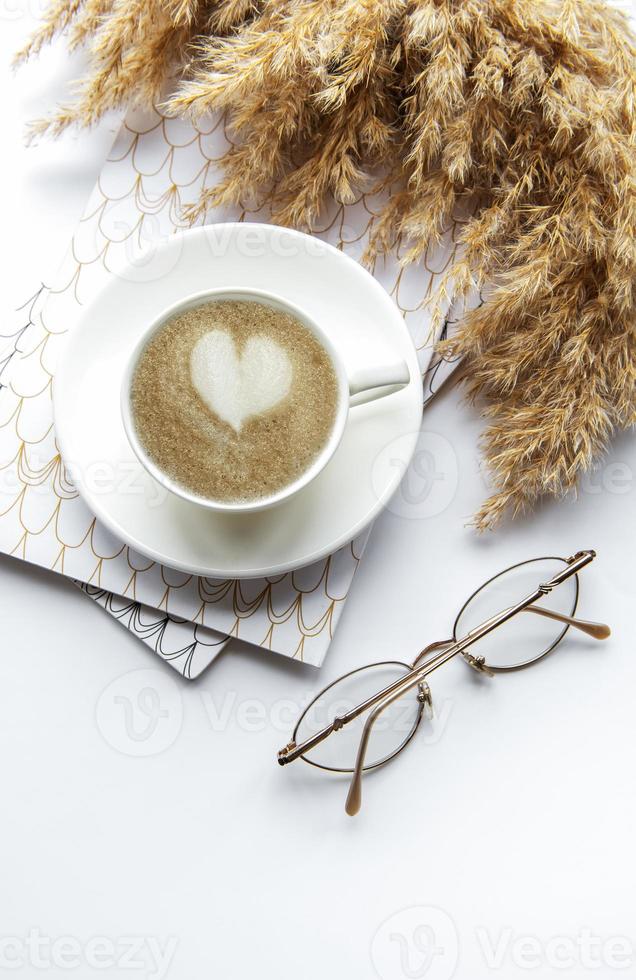 espacio de trabajo de escritorio de oficina con cuaderno, café y pasto de la pampa. foto