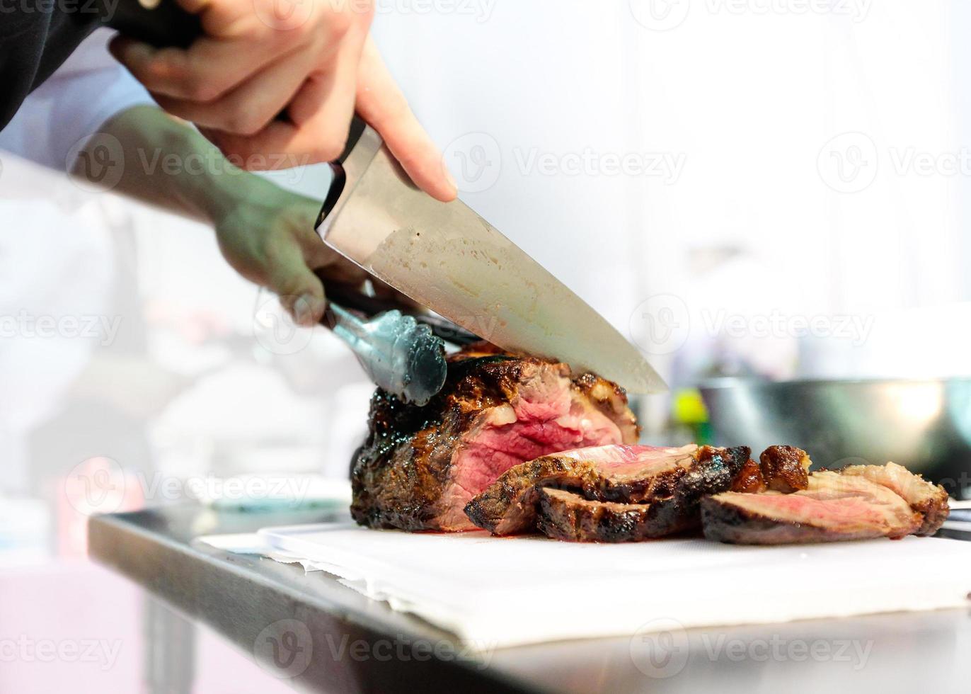 Chef con cuchillo y cortar sabroso bistec a la parrilla, chef en la cocina foto