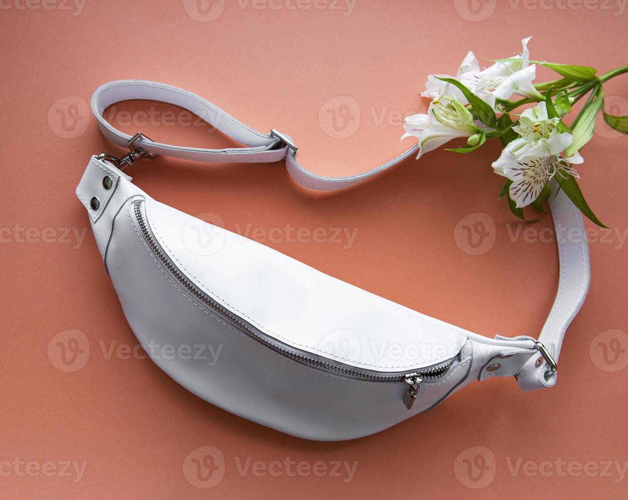 White belt leather bag and flowers on a light orange background photo