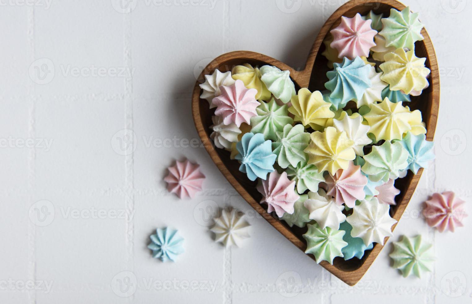 pequeños merengues de colores en el cuenco de madera en forma de corazón foto