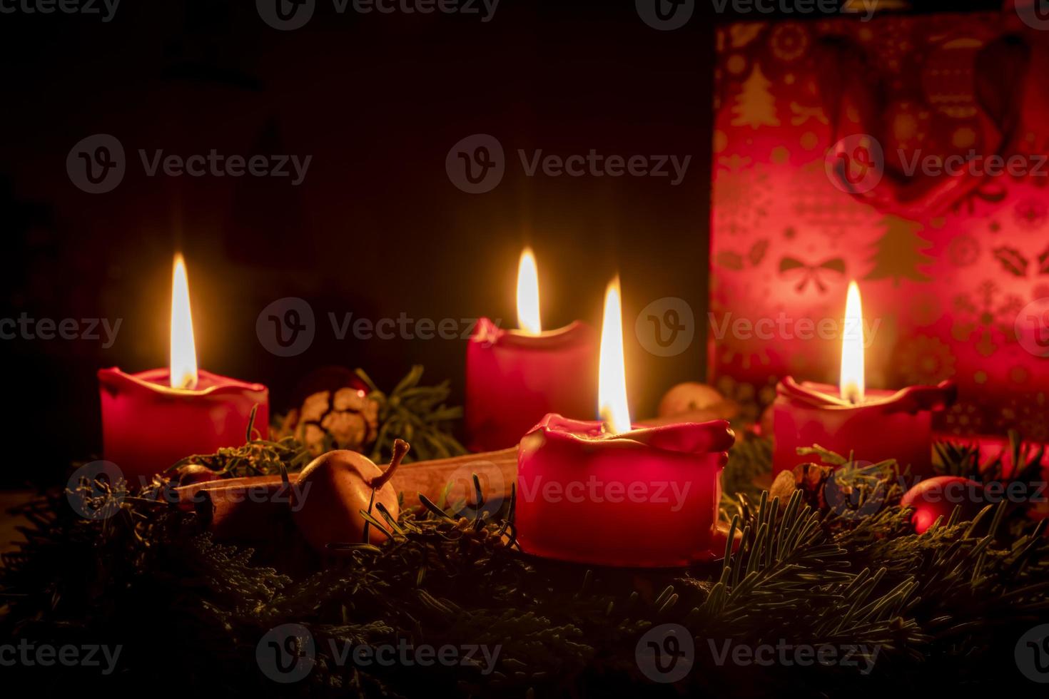 Corona de Adviento decorada hecha de ramas de abeto con velas rojas encendidas. foto