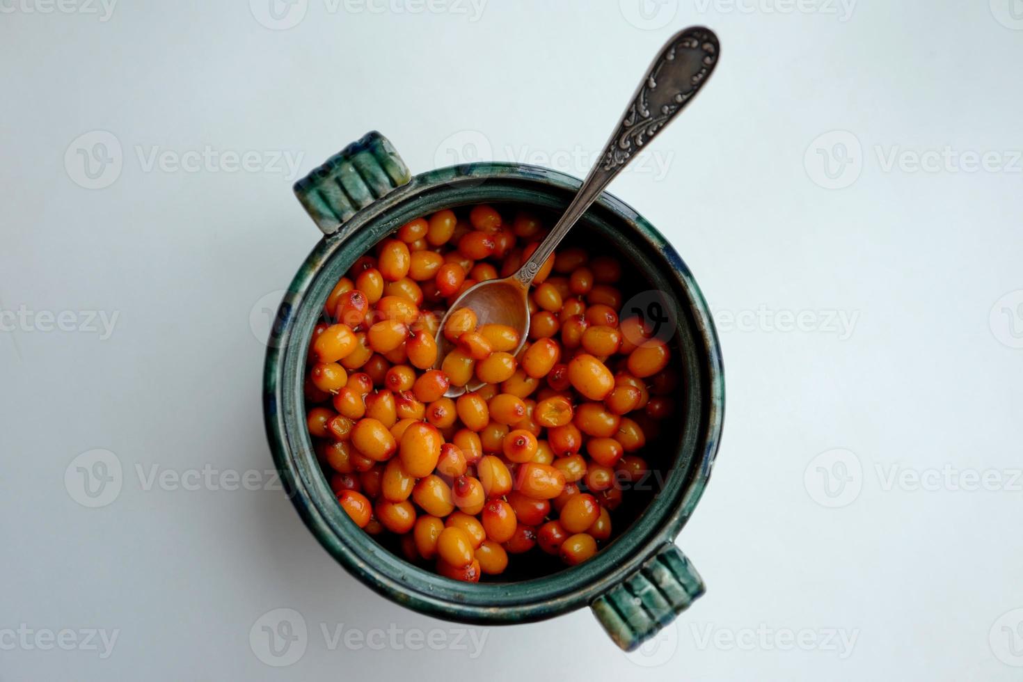Sea buckthorn berries in a green round cup with a teaspoon photo