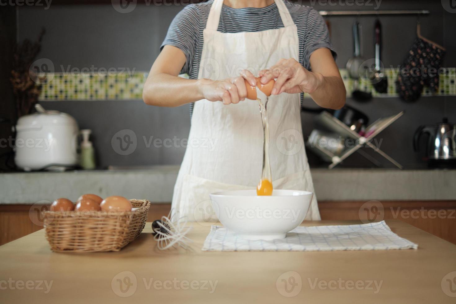 Female cook in a white apron is cracking an egg in home's kitchen. photo