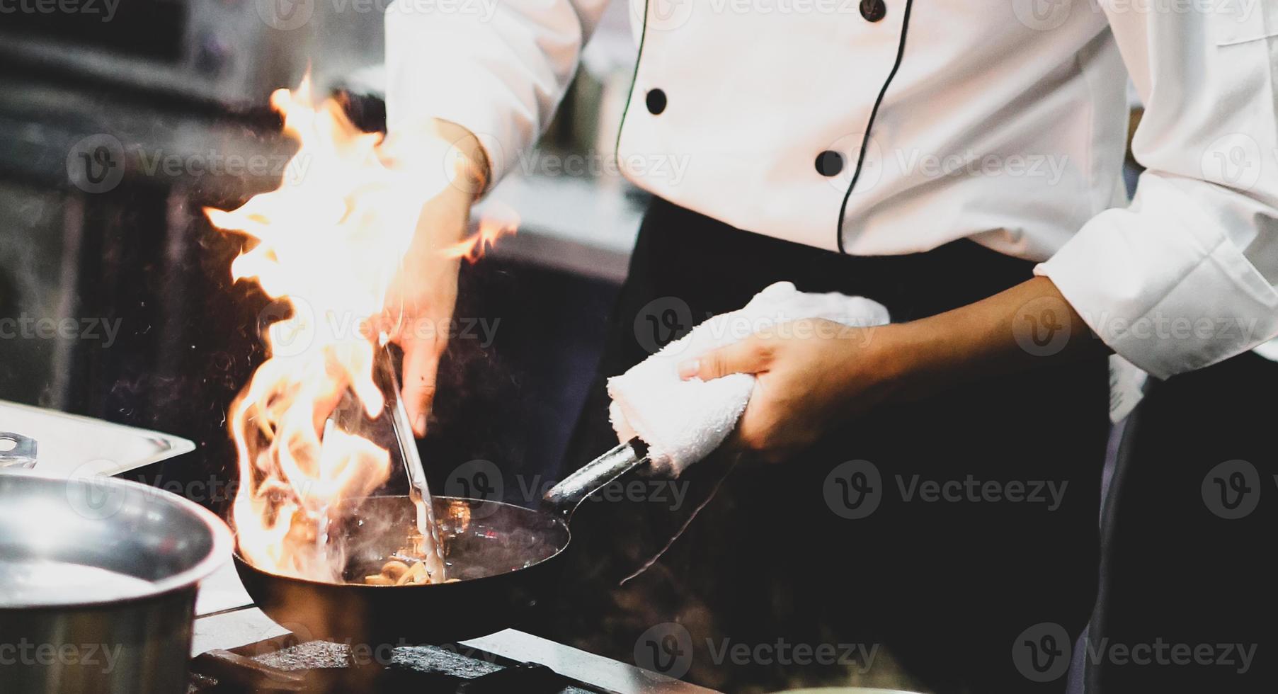 Chef cocinando con llama en una sartén sobre una estufa de cocina foto