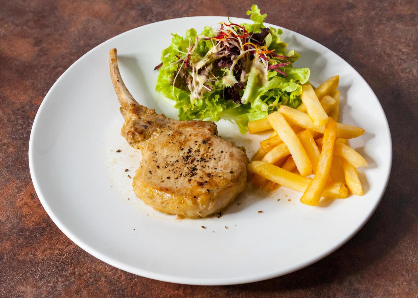 Chuletón de cerdo con ensalada y patatas fritas foto