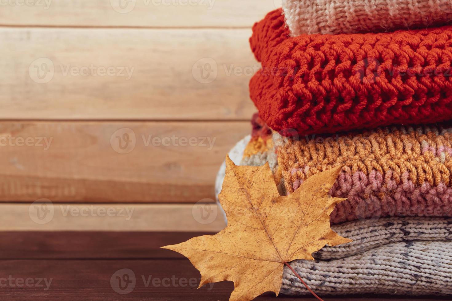 Stack of warm knitted sweaters. Woolen jumpers and maple leaf photo