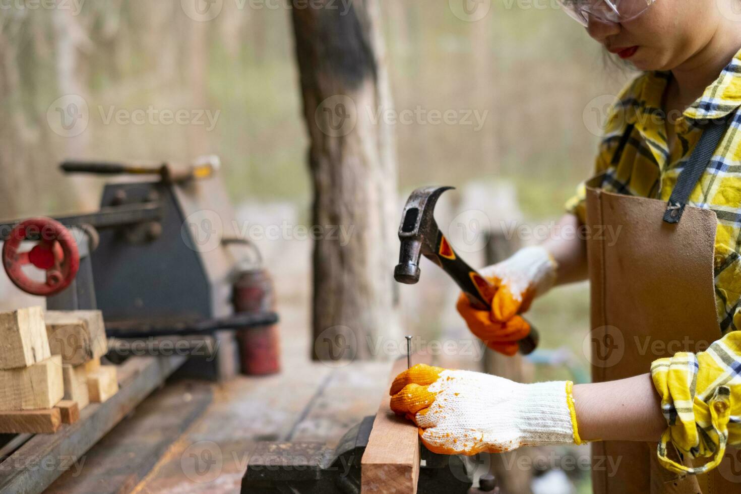 Mujer permanente trabajador constructor martillando clavos en la tabla de madera foto