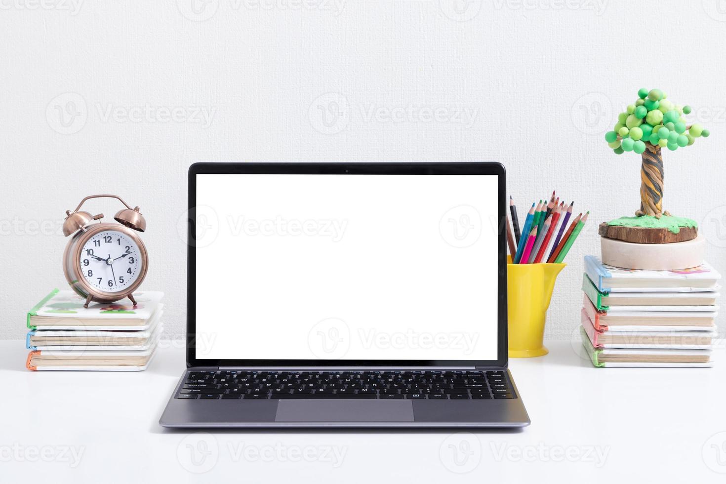 Open laptop mock-up at the child's workplace with book, alarm clock photo