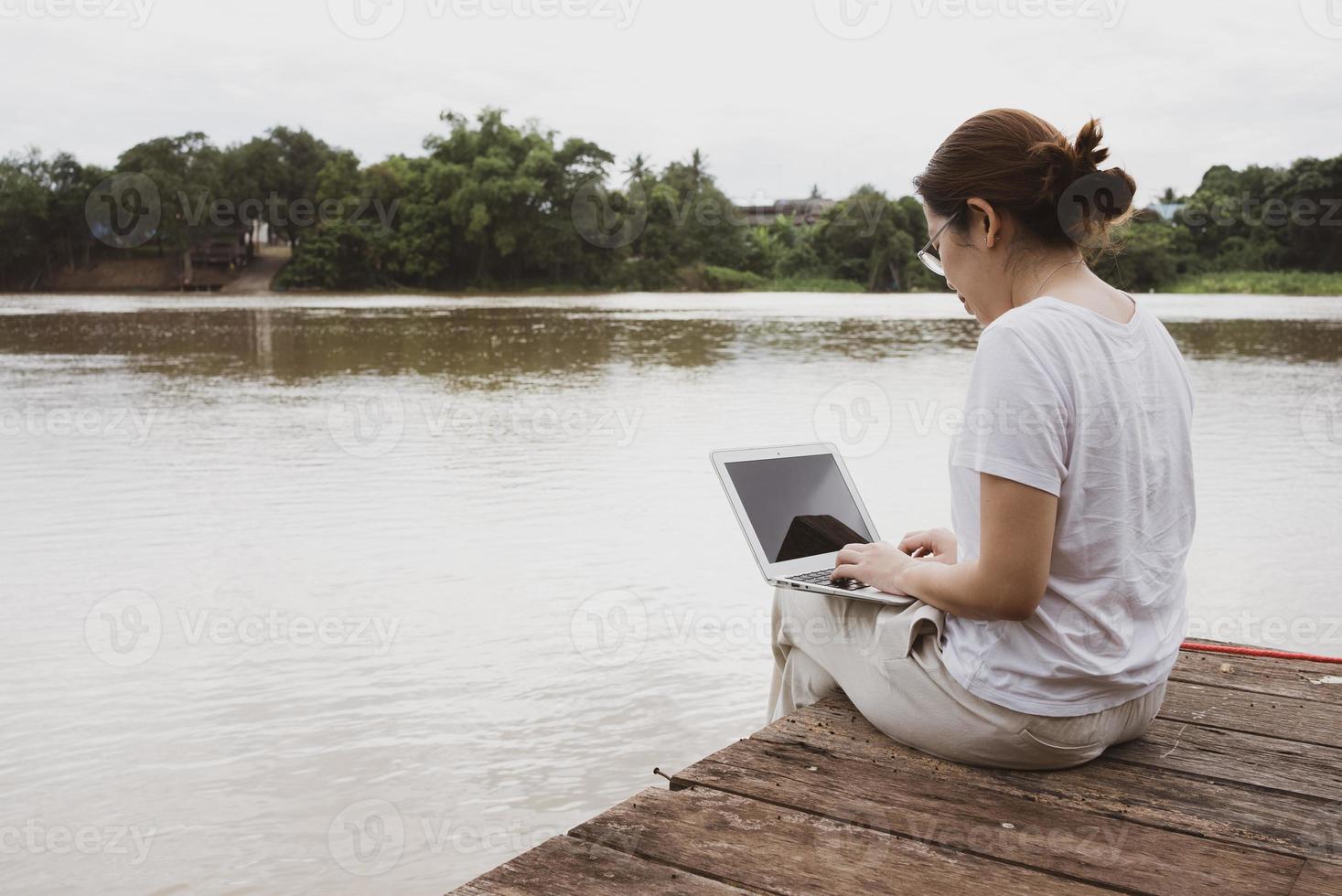 Adult woman using computer to work remotely from riverside photo
