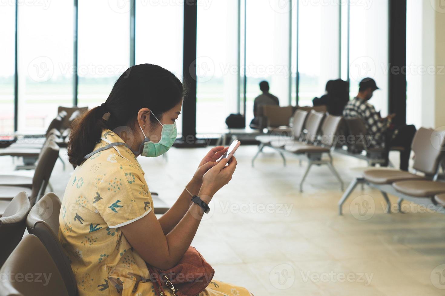 Joven mujer asiática sentada en el aeropuerto y con mascarilla foto