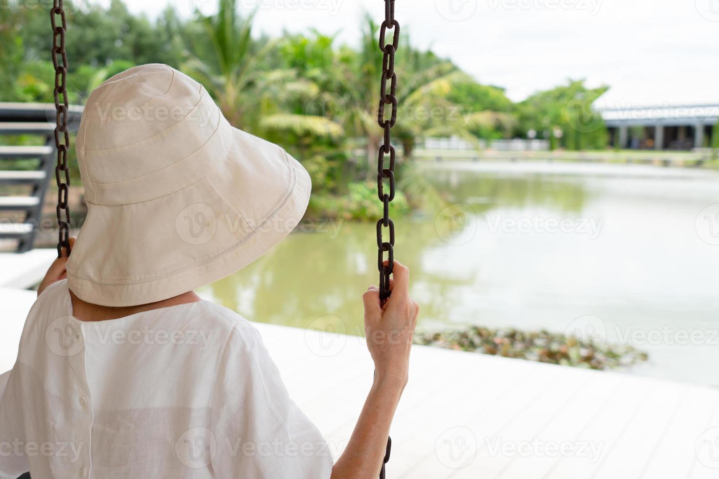 Mujer mayor sentada en un columpio y mirando al jardín y al lago foto