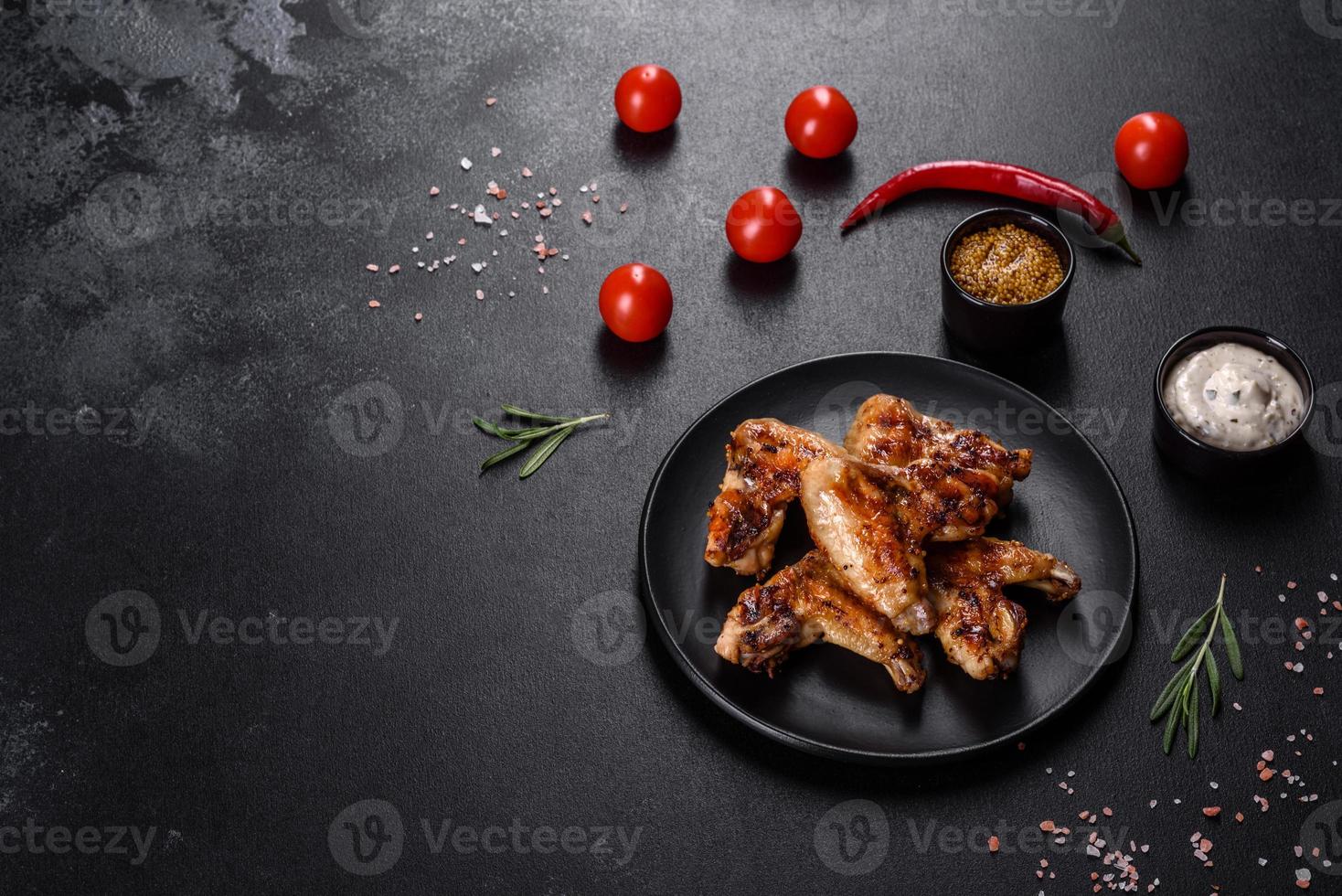 Alitas de pollo picantes a la parrilla sobre un fondo oscuro con especias y hierbas. foto