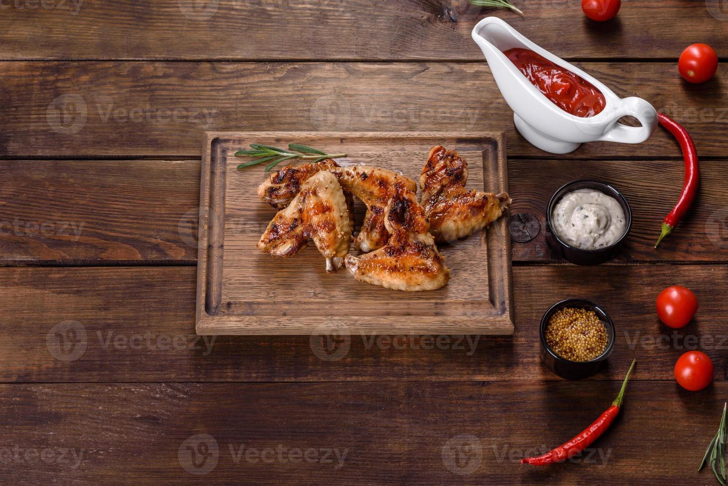 Alitas de pollo picantes a la parrilla sobre un fondo oscuro con especias y hierbas. foto