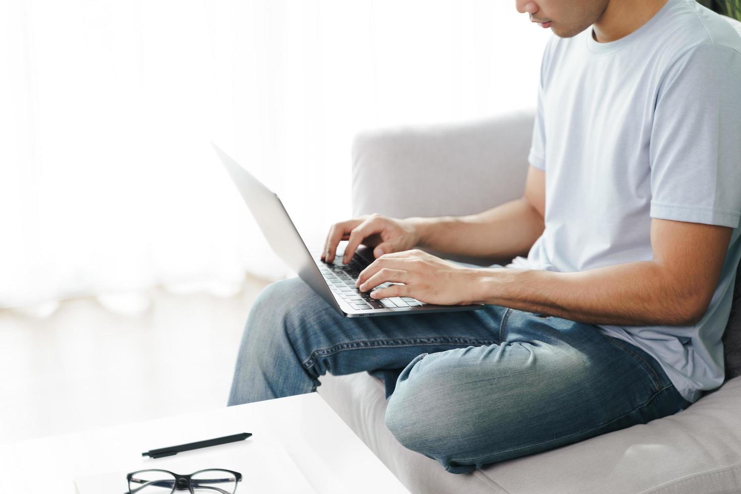 joven sentado en el sofá escribiendo en la computadora portátil para trabajar en línea. foto