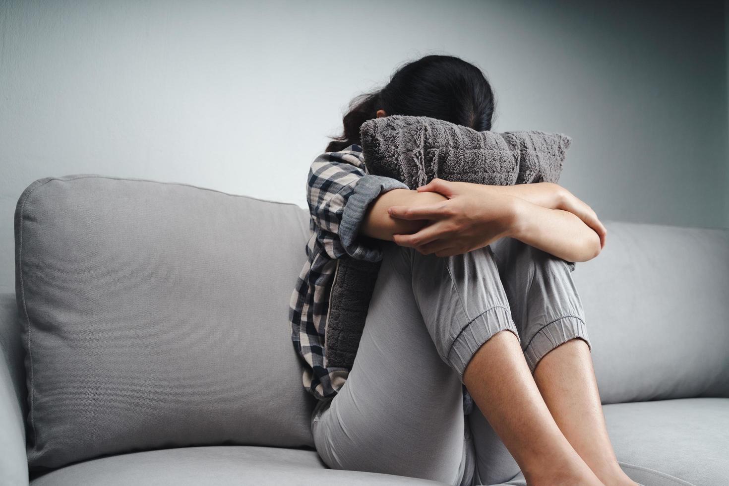 Sad woman is sitting on the couch and hiding her face on a pillow photo